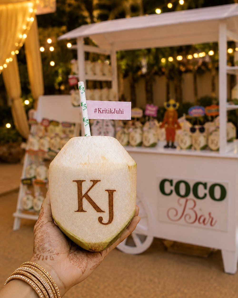 Hand with mehendi holding a KJ monogram engraved coconut with a hashtag straw flag at the Mr. Coconut Coco Bar